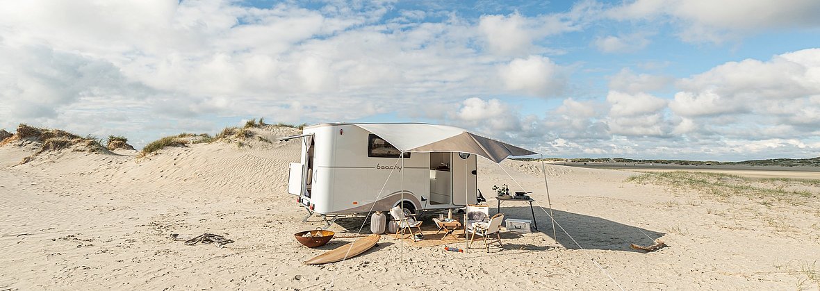 Ein Caravan steht am Strand, davor ist ein kleiner Sitzbereich mit Sonnensegel aufgebaut.