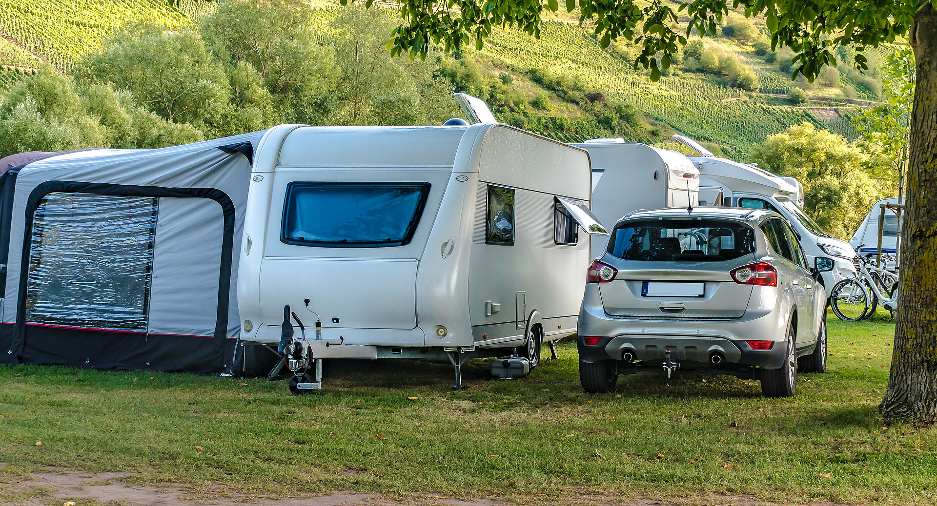 Ein Wohnwagen mit Vorzelt steht auf einem Campingplatz neben einem SUV.