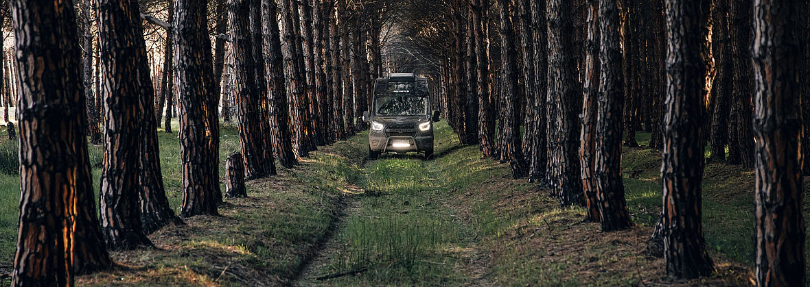 Ein Offroad-Wohnmobil fährt auf einem Feldweg durch den Wald.