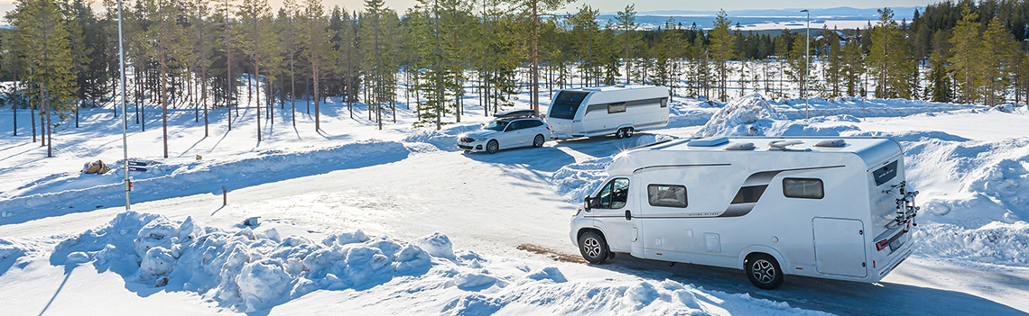 Ein Wohnmobil parkt an einer verschneiten Straße neben einem Berg.